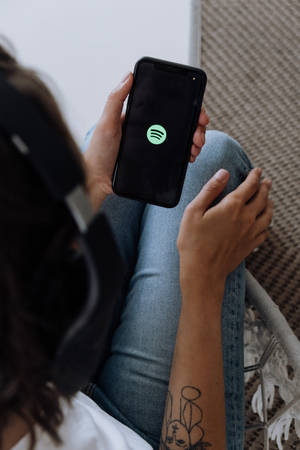 戴著耳機的人手持打開了Spotify應用程式的電話。