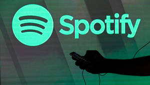 手在發光的Spotify標誌投影前拿著手機。