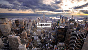紐約市天際線在黃昏時，雲層和燈火通明的摩天大樓上疊加著Supreme標誌。 — 紐約市 壁紙