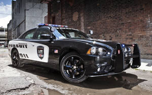 黑白警車停在磚牆附近的濕路面上。