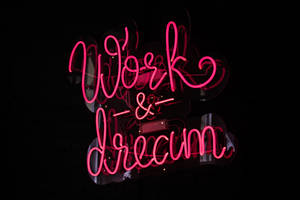 粉紅色霓虹燈牌，上面寫著 Work & Dream，掛在深色牆上。
