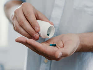 人從白色瓶子倒出一粒藍色膠囊到手掌中。