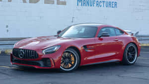 紅色 Mercedes-AMG GT R 跑車停放在磚牆附近的瀝青路面上。