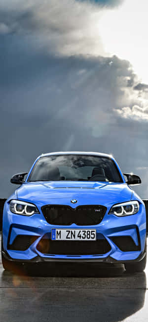 藍色BMW M2跑車停放在戲劇性的日落雲層下。 — iPhone 18 Pro Max 壁紙