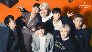 七位K-pop偶像穿著時尚服裝，在橙色背景的舞台上一起擺姿勢。