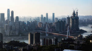 在朦朧的天空下，一座密集城市的全景，河流上有一座曲線橋和高樓大廈。 — 唐人街 GIF 壁紙