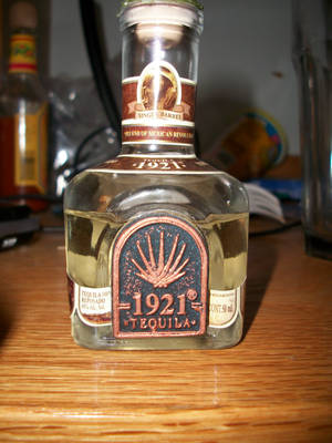在昏暗房間的木桌上，一個1921 Tequila reposado酒瓶。