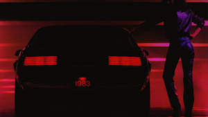 一個人站在一輛1983年保時捷旁邊，車尾燈發出紅色光芒，在霓虹紅光中。
