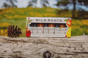 黃色花田中，一盒 Wild Roots 調味伏特加放在木頭上，旁邊有松果