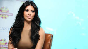 Kim Kardashian 在活動中坐在皮椅上，背景為藍綠色。