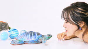 女士仔細看著白色桌子上的一個藍綠色烏龜雕像。