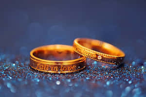 兩枚金結婚戒指，刻有「fall in love」，在藍色閃粉上。