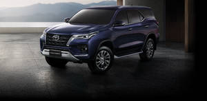 深藍色豐田 Fortuner SUV 停放在混凝土平台上，俯瞰山脈和海洋。 — 汽車 壁紙