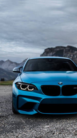 多雲天空下，碎石上靠近山巒的藍色BMW M2跑車