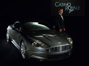 丹尼爾·基克身穿禮服站在銀色Aston Martin DBS旁，在攝影棚燈光下。 — 電影 GIF 壁紙