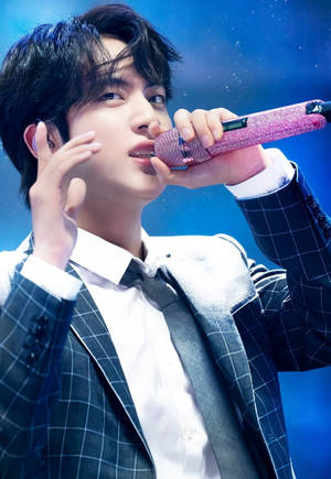 男性K-pop歌手在舞台上表演，手持閃亮粉紅色麥克風，搭配藍色燈光。