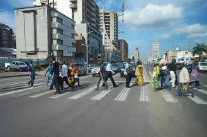 一群行人橫過有車輛同高樓大廈嘅城市街道。