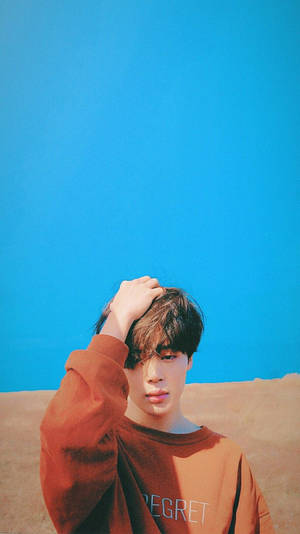 穿著鏽色運動衫的年輕男子在明亮的藍天下沙漠中觸摸頭髮 — Jimin GIF 壁紙