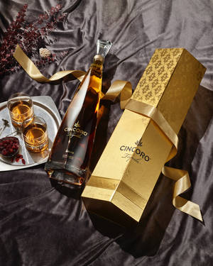 Cincoro龍舌蘭酒瓶和禮盒，附品酒杯，置於深色緞面上。