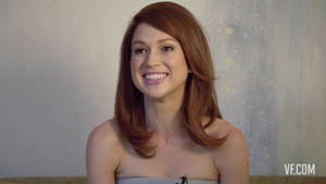 一位微笑的紅髮女性在中性室內環境中。