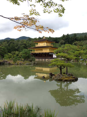 金色寺廟亭閣倒映在靜止的池塘中，周圍有綠樹和山丘。 — 2048x2732 壁紙