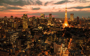 黃昏時分的東京城市景觀，燈火通明的建築物和東京塔在色彩繽紛的天空下閃耀。 — 日落大道 壁紙