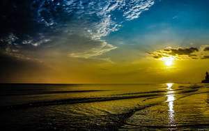 夕陽映照海面，燈塔剪影與金色水光反射。 — 海灘日落 壁紙
