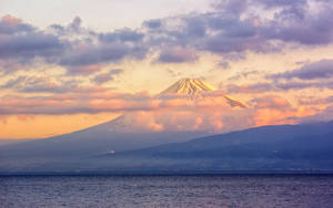 日落時的富士山，雪峰和色彩斑斕的雲彩，下方是平靜的海洋