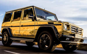 金色 Mercedes G-Class SUV 在海岸公路上行駛，背景是海洋。
