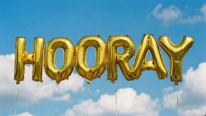 金色 'HOORAY' 氣球在藍天白雲中漂浮。