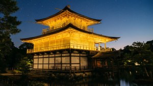 金色寺廟亭閣在夜間亮起，上方有星星，下方有水。