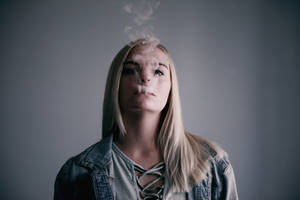 年輕女性在灰色背景的攝影棚中呼出蒸氣。