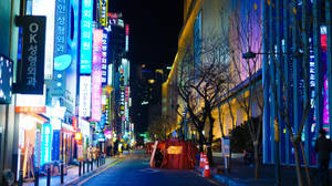 夜晚的城市街道，被色彩繽紛的霓虹招牌和光禿禿的樹木照亮。 — 夜景城市 壁紙