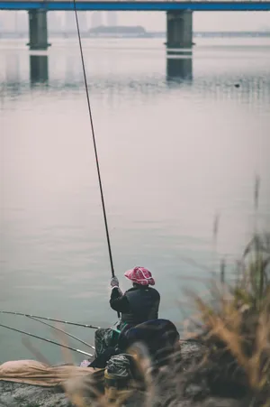 喺河岸釣魚嘅人,背景有橋