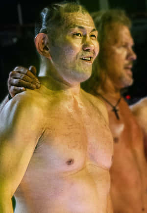 兩個汗流浹背的男人在溫暖的舞台燈光下微笑，其中一個把手放在肩膀上。
