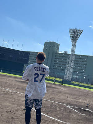棒球運動員穿著Suzuki 27號球衣，在陽光明媚的球場上面對體育場。