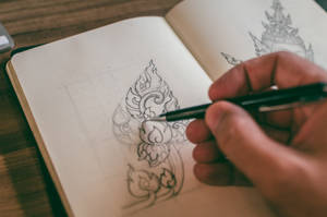 手用黑色筆在素描本上繪畫華麗的泰式圖案。