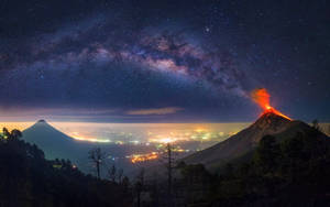 夜間火山爆發，熔岩在星空和遠處城市燈光下流淌。