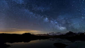 積雪的山峰和湖泊在星空下倒映，銀河系清晰可見。 — 夜空 壁紙