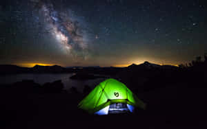 一個發光的綠色帳篷，在星空下，銀河在湖泊上方可見。