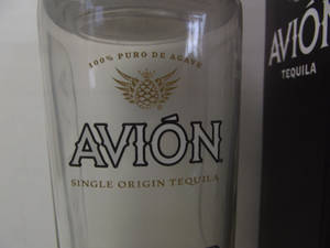 Avión龍舌蘭酒杯和酒瓶，帶有金色和黑色品牌標識。 — 4:3 壁紙