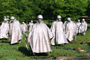 銀色嘅士兵雕像穿著斗篷，喺有綠樹嘅草地公園上行進。 — 陣亡將士紀念日 GIF 壁紙