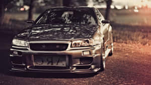 銀色日產Skyline R34飄移車停泊在碎石路上，正值黃金時段。