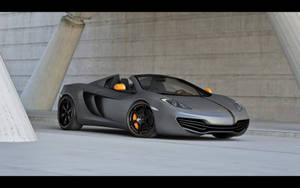 磨砂灰色McLaren跑車帶有橙色細節，停在混凝土結構中。