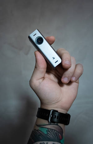 手拿銀色運動相機，有紋身手腕和黑色手錶。