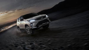 銀色豐田RAV4 Legend在暮色中行駛在碎石路上，遠處有城市燈光。