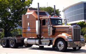 橙色Kenworth半掛卡車停在城市街道上，背景有樹木和玻璃建築。 — 林寶堅尼貨車 壁紙