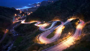 夜晚蜿蜒的海岸道路，帶有移動汽車的發光車燈軌跡。