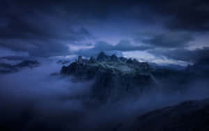暮色中，山峰聳立於霧氣繚繞的雲層之上。 — 2880x1800 壁紙