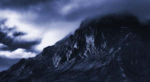 暴風雲下的黑暗山脈，帶有藍色和白色燈光。 — 夜空 壁紙